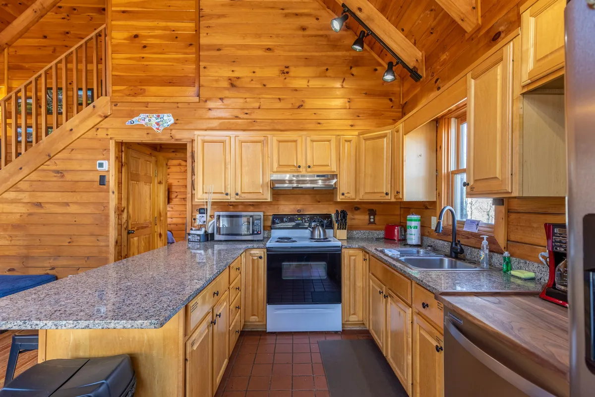 A close-up view of the kitchen focusing on the granite countertop, wooden cabinetry, and modern kitchen appliances. The layout encourages cooking and communal experiences, emphasizing the breakfast bar and open workspace.