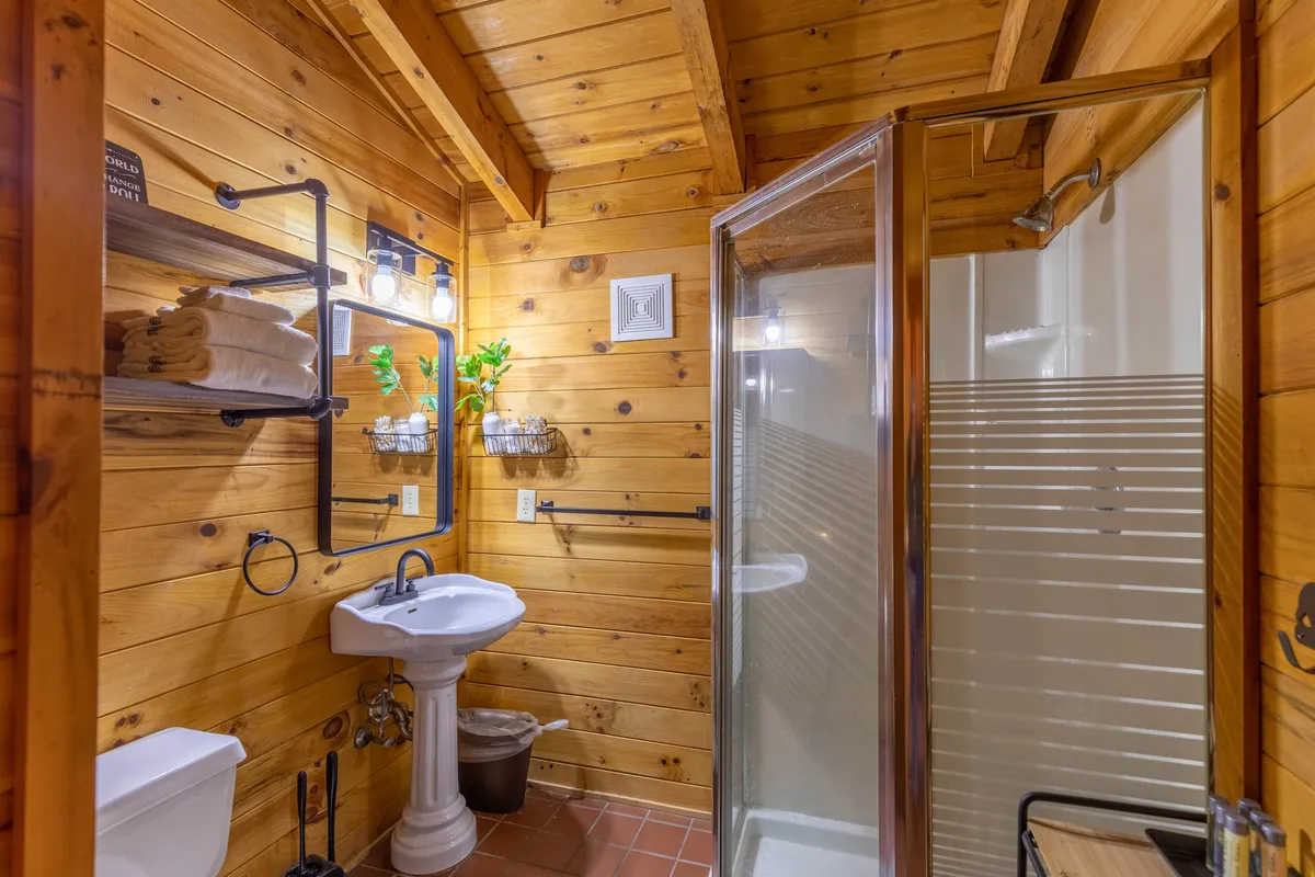 A clean, inviting bathroom with wooden walls, a modern shower area, a sink and mirror, and neatly arranged shelves with towels. The lighting is warm and the details suggest a comfortable space for refreshing after outdoor adventures.